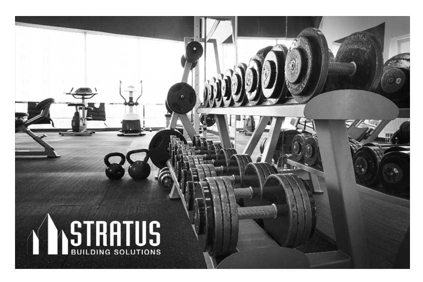 A rack of dumbbells at a gym with two kettleballs on the ground and equipment in the background