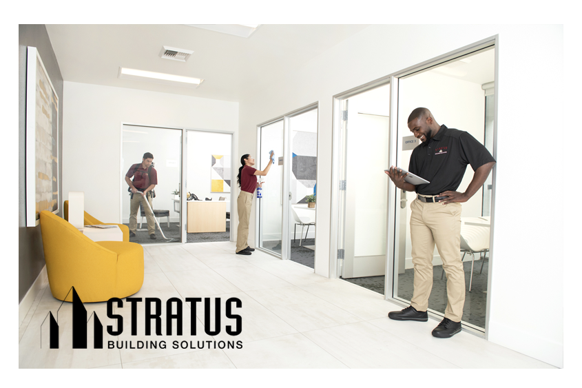 A Stratus Franchise Owner Smiles and Looks at a Tablet While Two Workers in the Background Vacuum and Wipe a Sliding Glass Door 