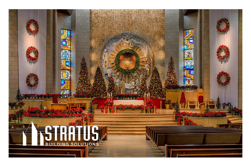 The Interior of a Church Decorated for Christmas with Trees and Wreaths Pictured from Behind the Pews Looking at the Stage