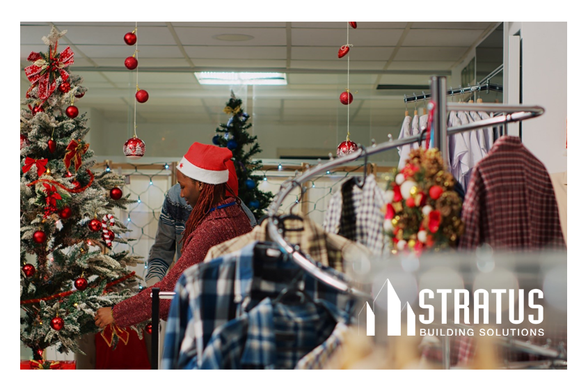 A rack of clothes in front a Christmas tree and a retail worker decorating a store for Christmas. 