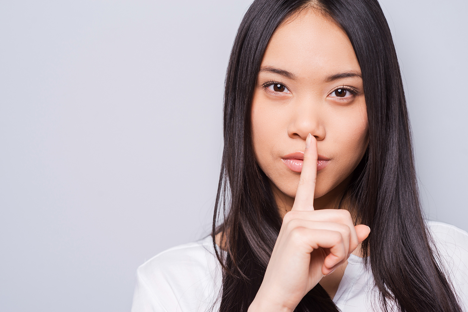 a dark haired woman in white telling a secret with a gray background