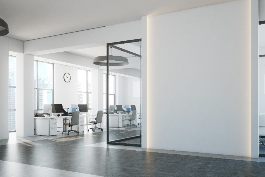 An office building with grey floors, white walls, large windows, and chairs with desks and computers. 