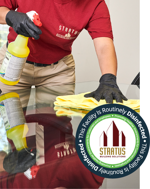 Stratus worker cleaning a glass table with green chemicals and a microfiber cloth. 