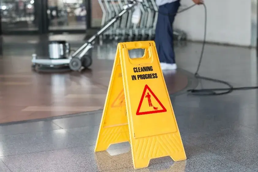 Yellow caution sign in front of person deep cleaning the floor of an office