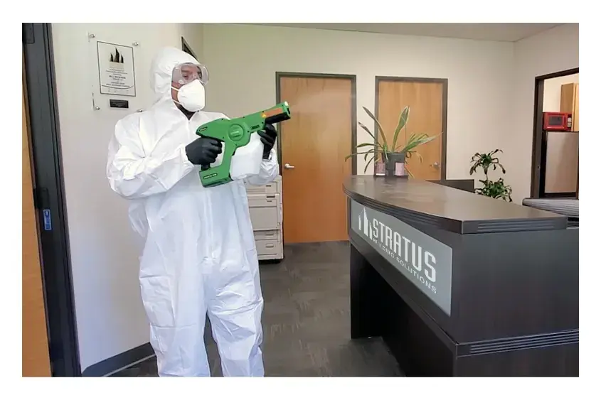 A Stratus Employee in a Uniform Shirt, Goggles, and Face Mask Uses a Disinfecting Machine to Spray an Office Reception Desk