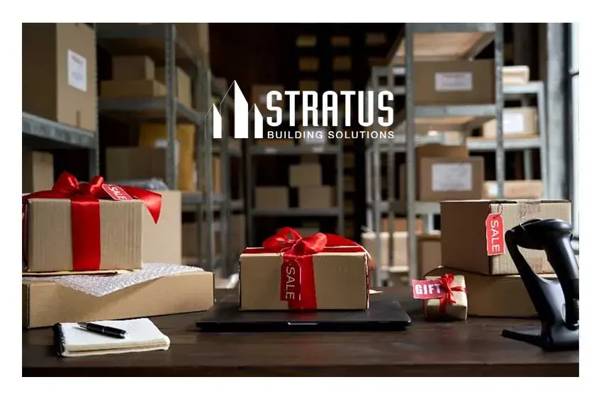 A warehouse stocked with boxes on shelves, two boxes wrapped in red ribbons on a desk.