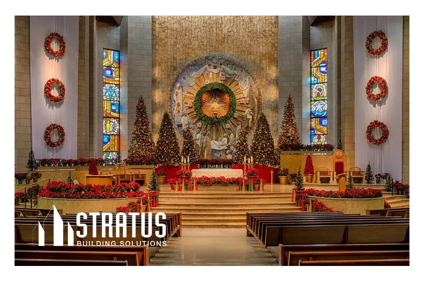 The Interior of a Church Decorated for Christmas with Trees and Wreaths Pictured from Behind the Pews Looking at the Stage